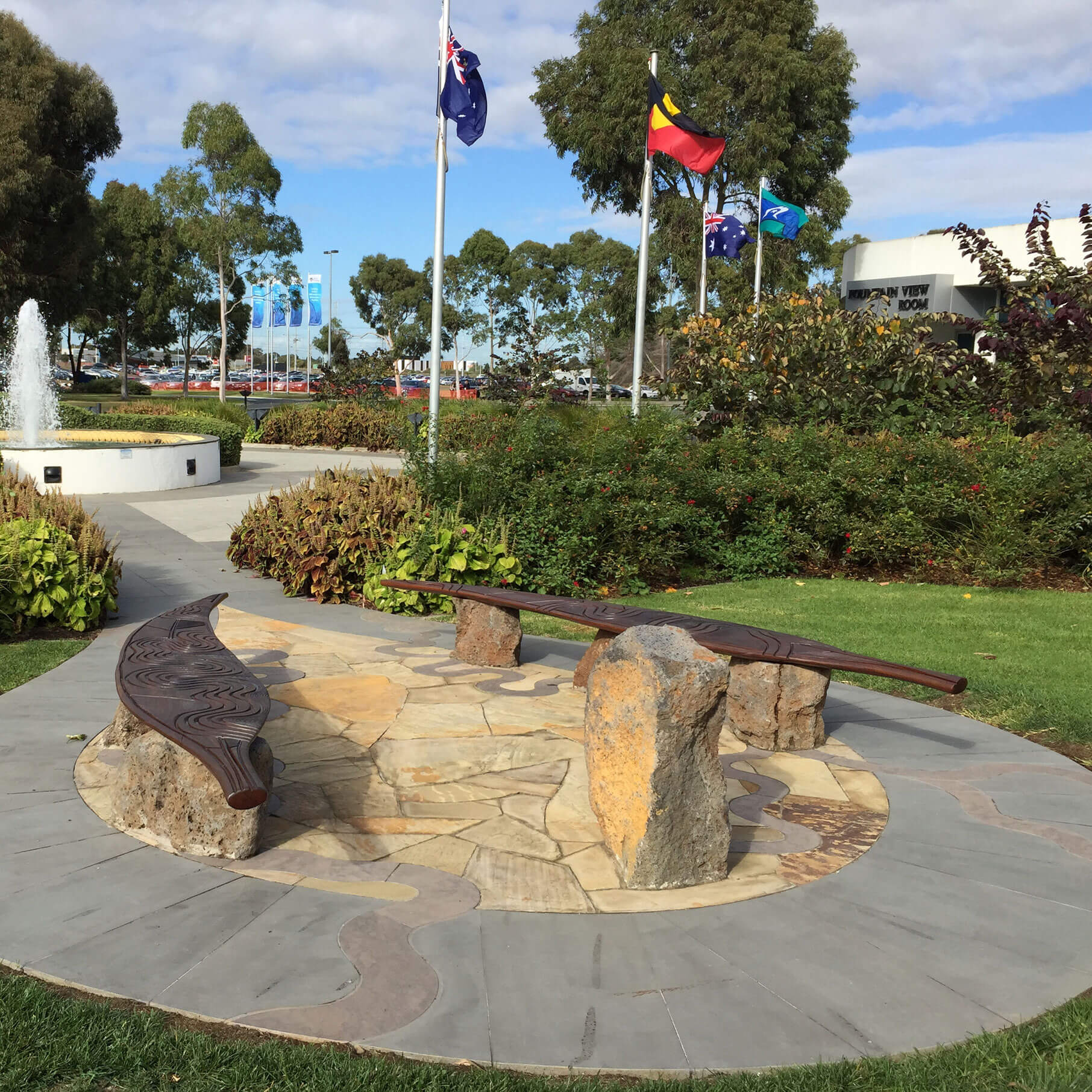 A park with Australian, Aboriginal, and Torres Strait Islander flags, featuring a stone path and wooden benches.
