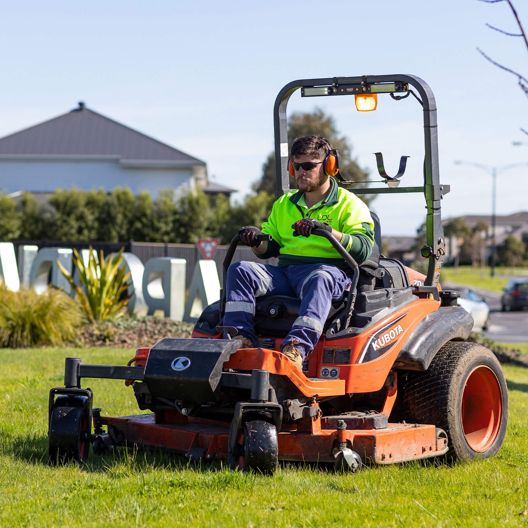 A landscape worker on a ride-on mower cutting grass in a new housing estate.