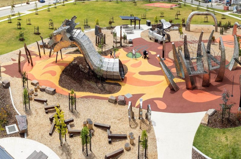 Steel dragon head sculpture in the middle of a landscaped park with a playground